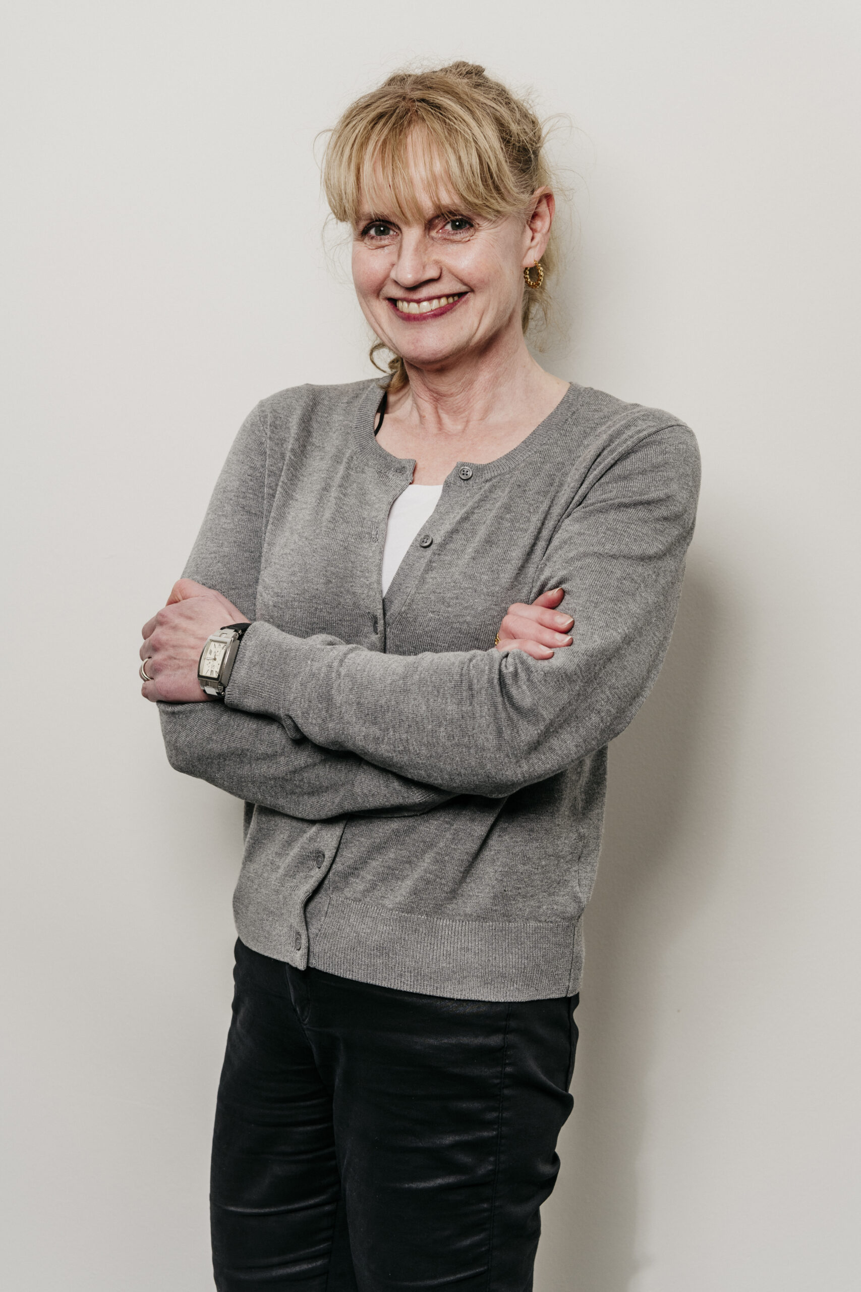 Vrouw glimlachend in grijze trui Fysio loon op zand.