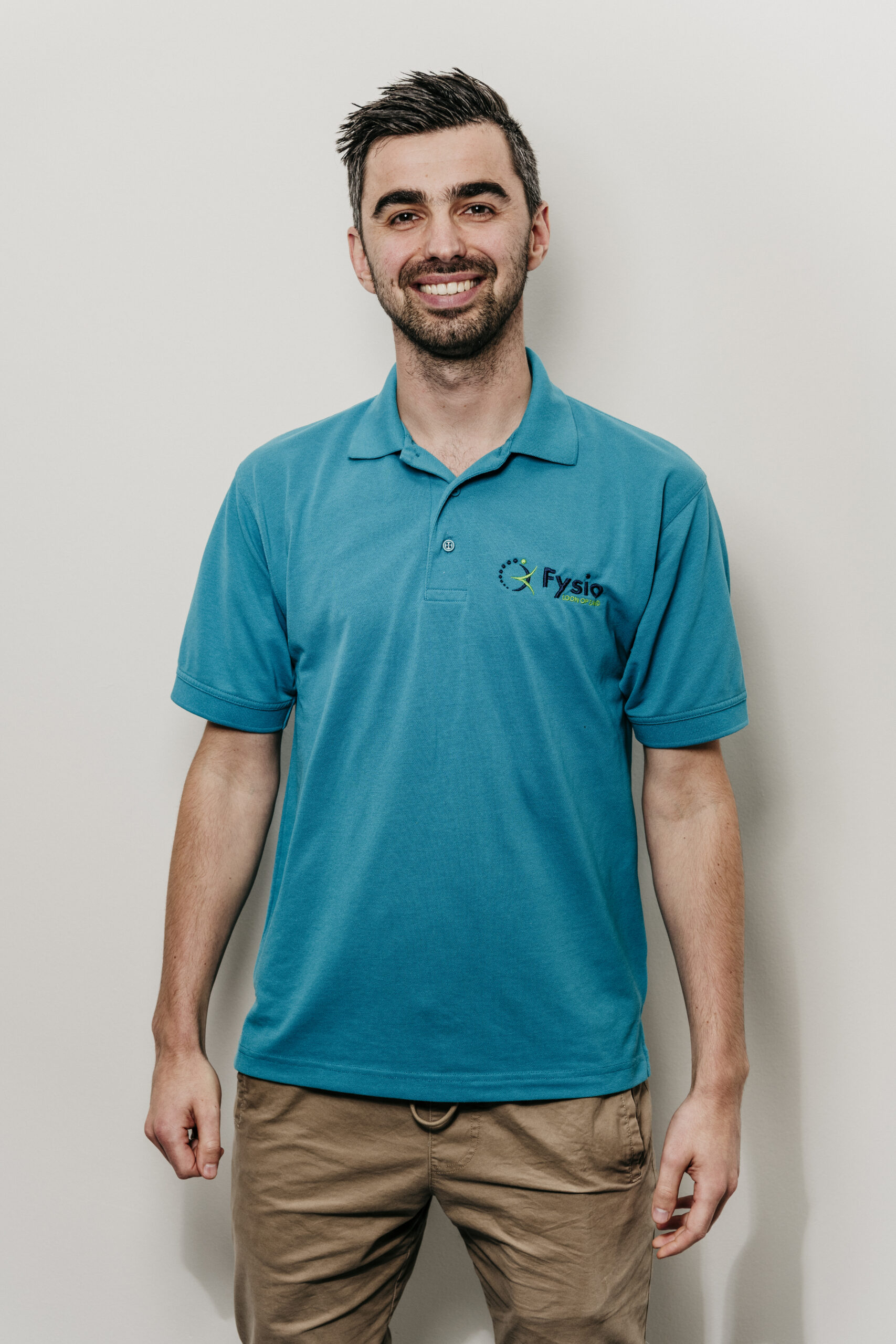 Man met blauwe polo glimlacht Fysio loon op zand
